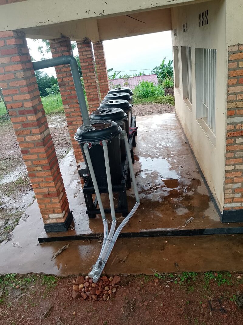 Amazi tanks on a raised stand along a house wall, fed by downpipes from the roof